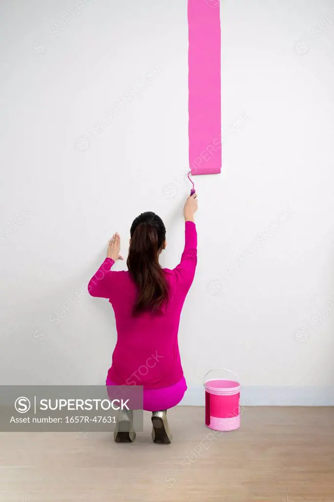 Woman painting a wall with a pink color