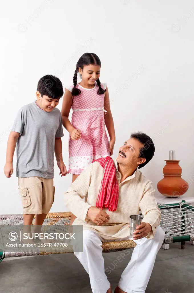 Farmer sitting on a cot with his children standing behind him