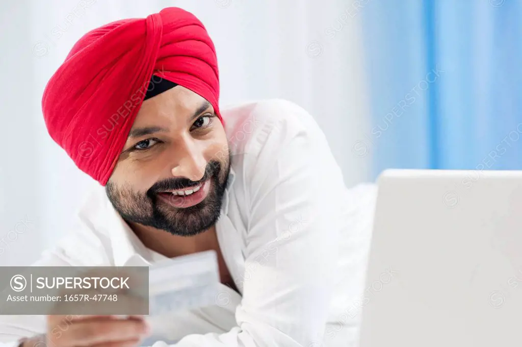 Smiling Sikh man doing online shopping with a credit card