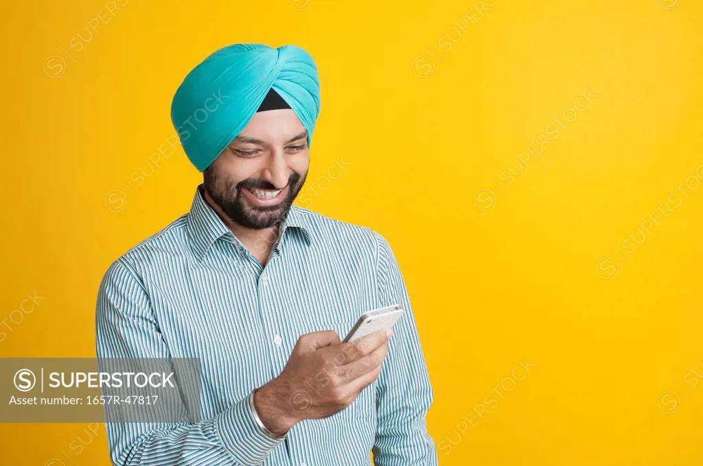 Sikh man reading messages on a mobile phone and smiling