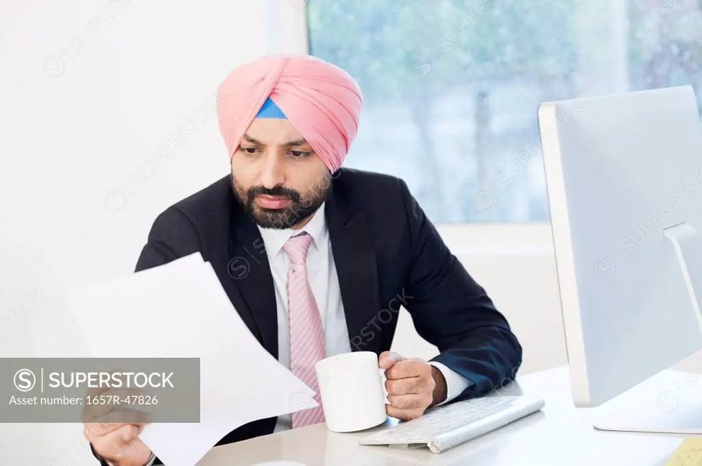 Businessman reading a document while drinking coffee in an office