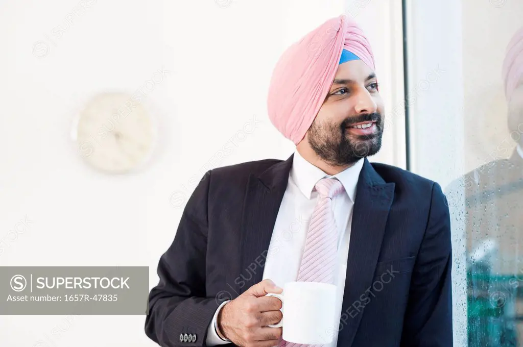 Businessman looking out of a window while drinking coffee