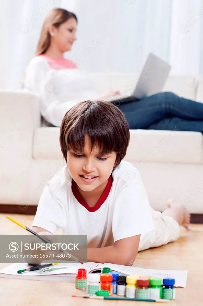 Boy making a painting with his mother using laptop in the background