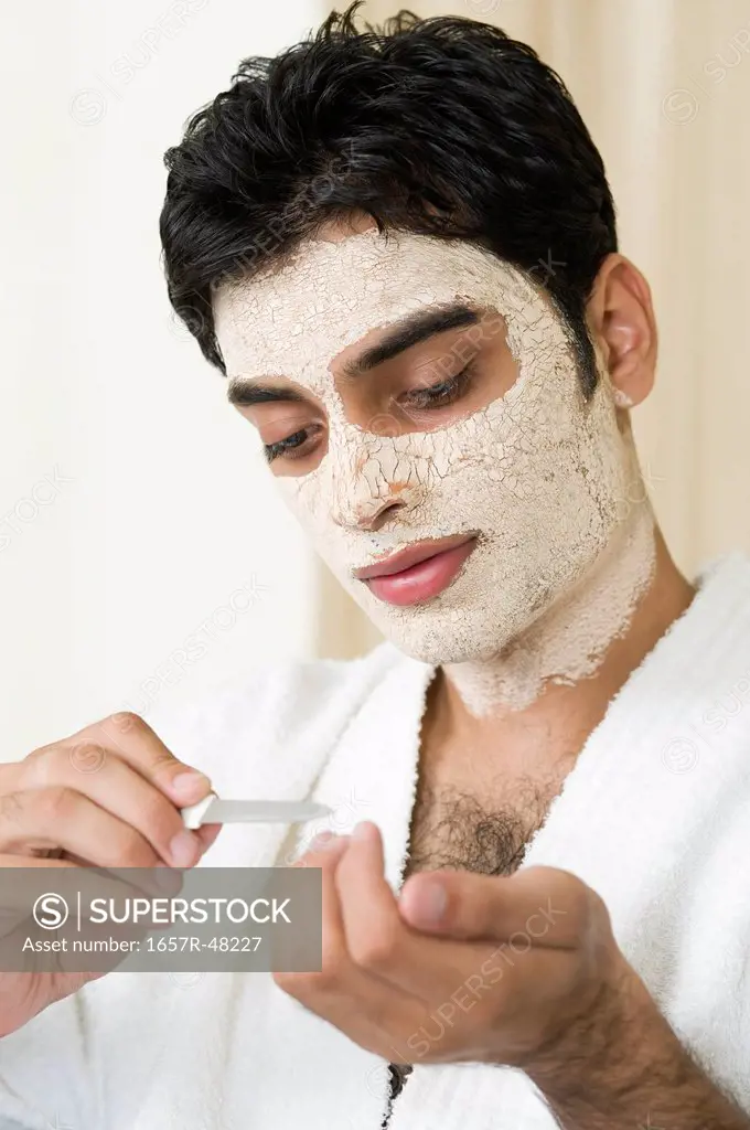 Close-up of a man with facial mask and filing his nails