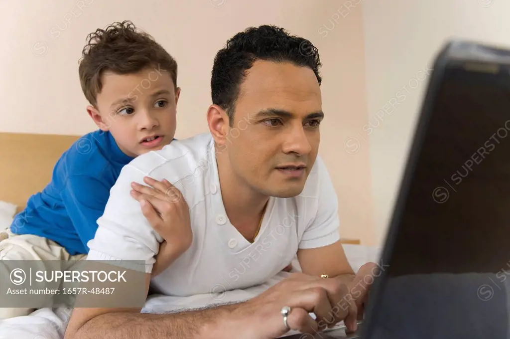 Man using a laptop with son hugging him from behind