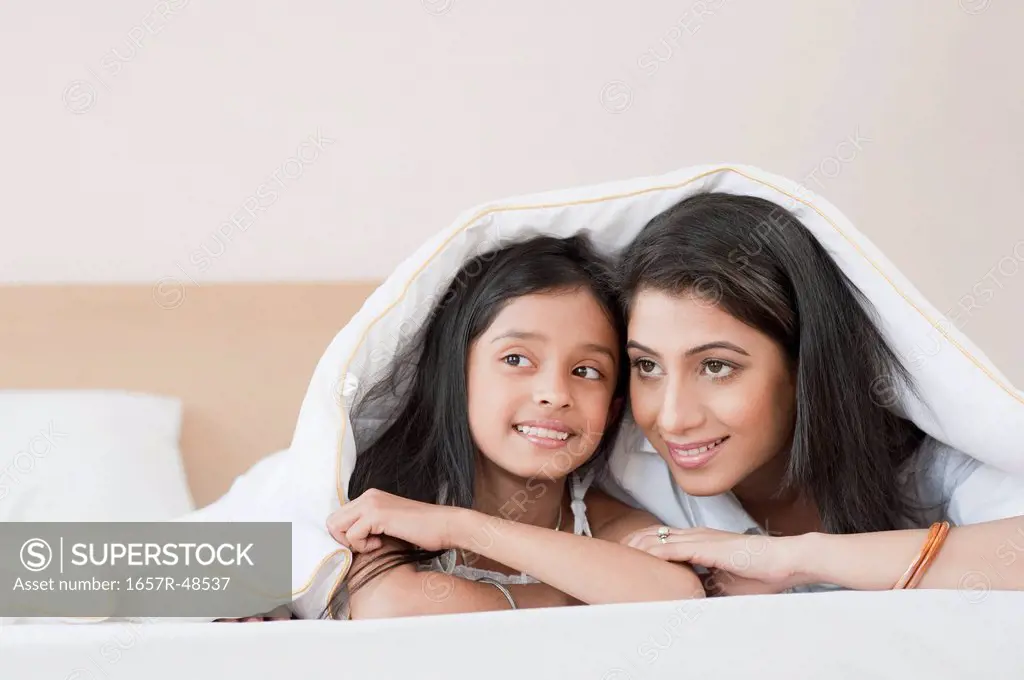 Woman and her daughter lying on the bed under a blanket