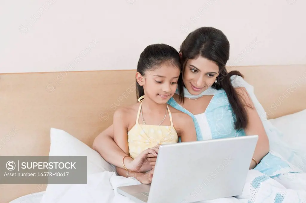 Woman and her daughter using a laptop on the bed