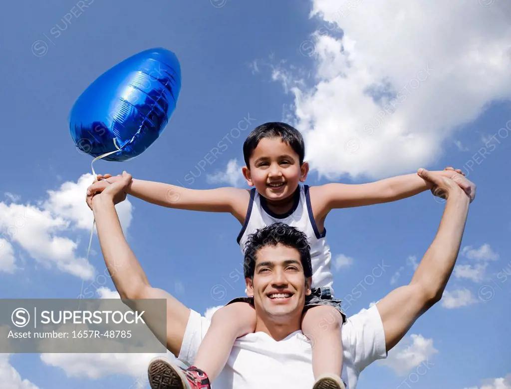 Man carrying his son on shoulders holding a balloon, Gurgaon, Haryana, India