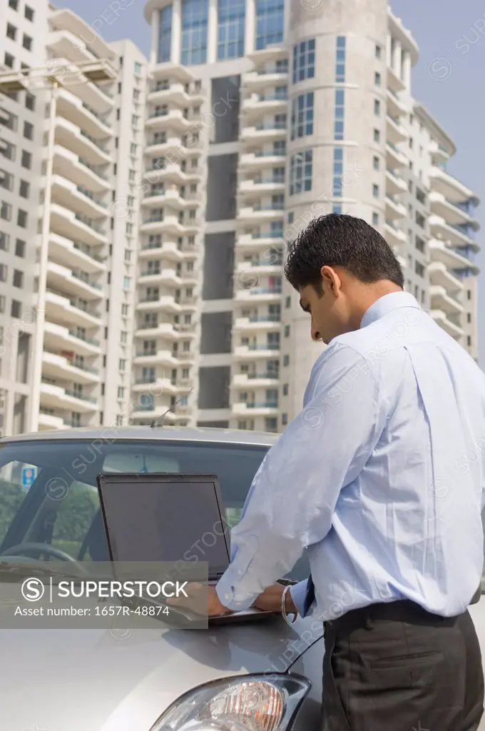 Businessman working on a laptop on a car hood, Gurgaon, Haryana, India