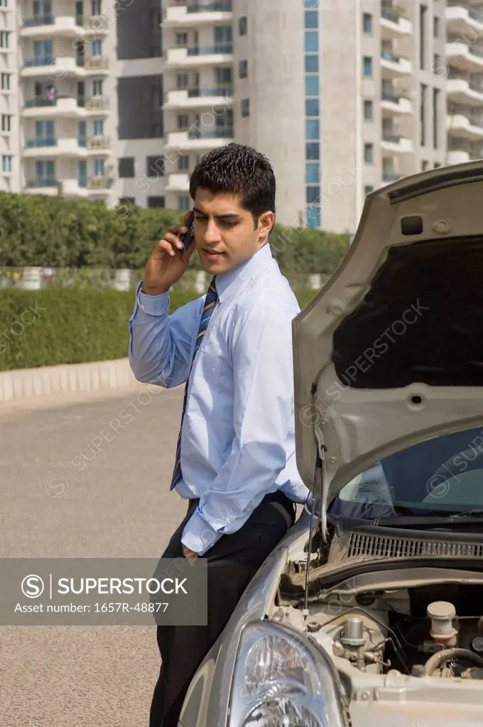Businessman standing near a broken down car and talking on a mobile phone, Gurgaon, Haryana, India