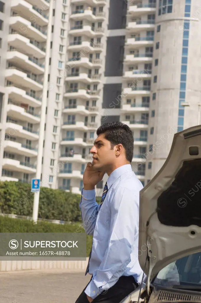 Businessman standing near a broken down car and talking on a mobile phone, Gurgaon, Haryana, India