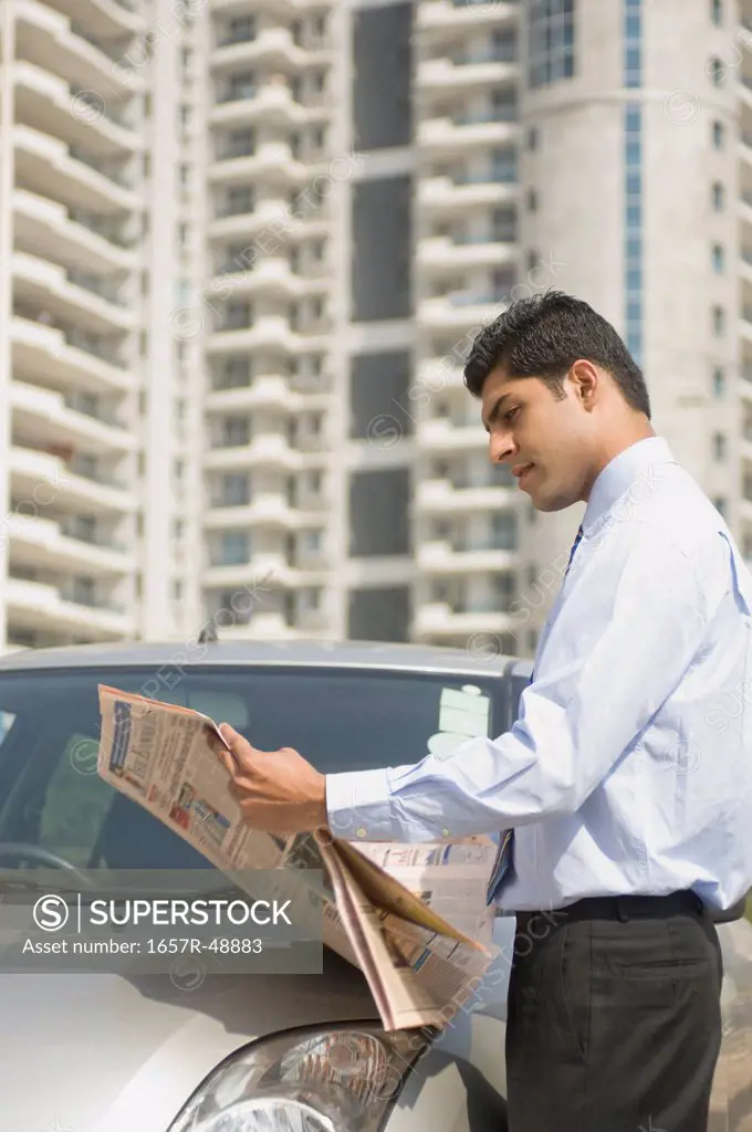 Businessman reading a newspaper beside a car, Gurgaon, Haryana, India