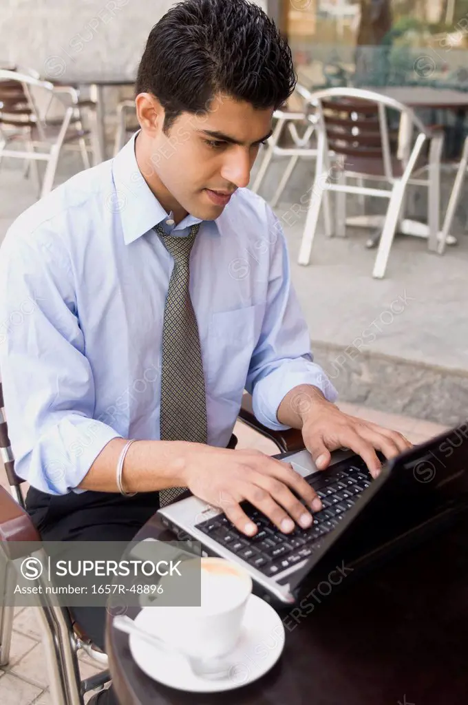 Businessman using a laptop at a sidewalk cafe, Gurgaon, Haryana, India