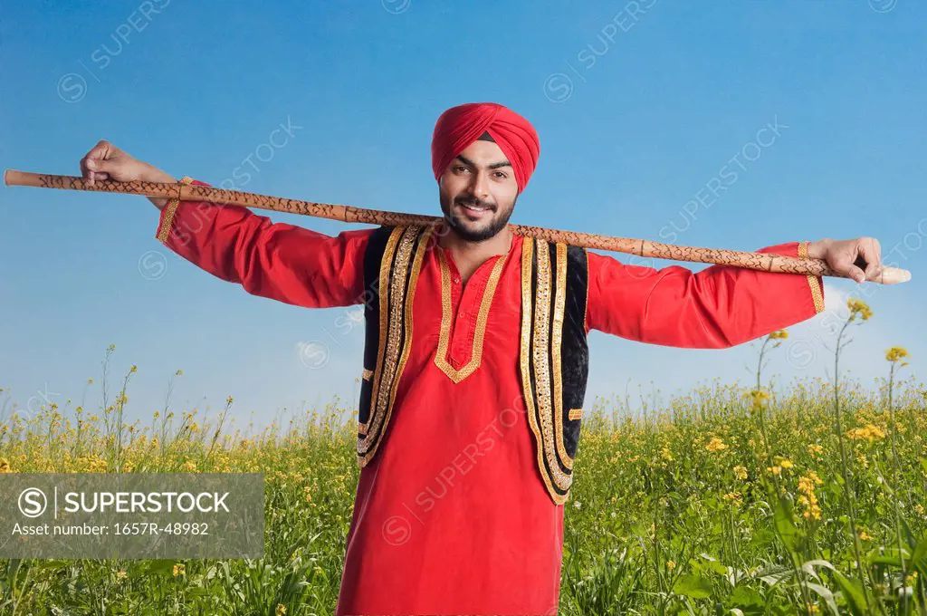 Man holding a stick and smiling in a field, Gurgaon, Haryana, India