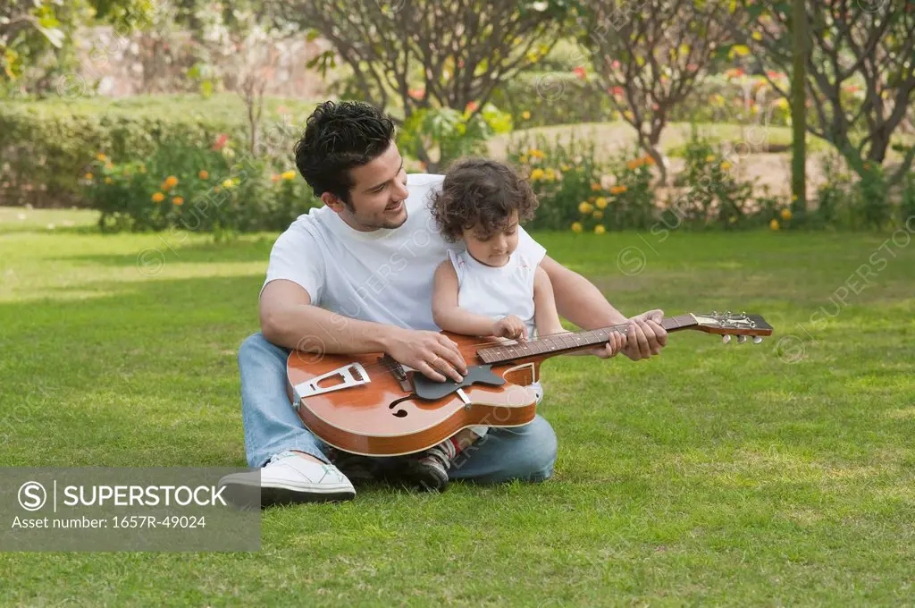 Man playing a guitar with his son sitting on lap