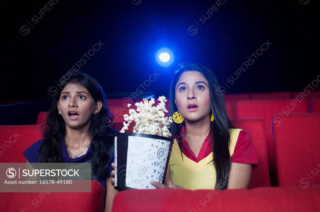 Two female friends looking surprised while watching movie in a cinema hall