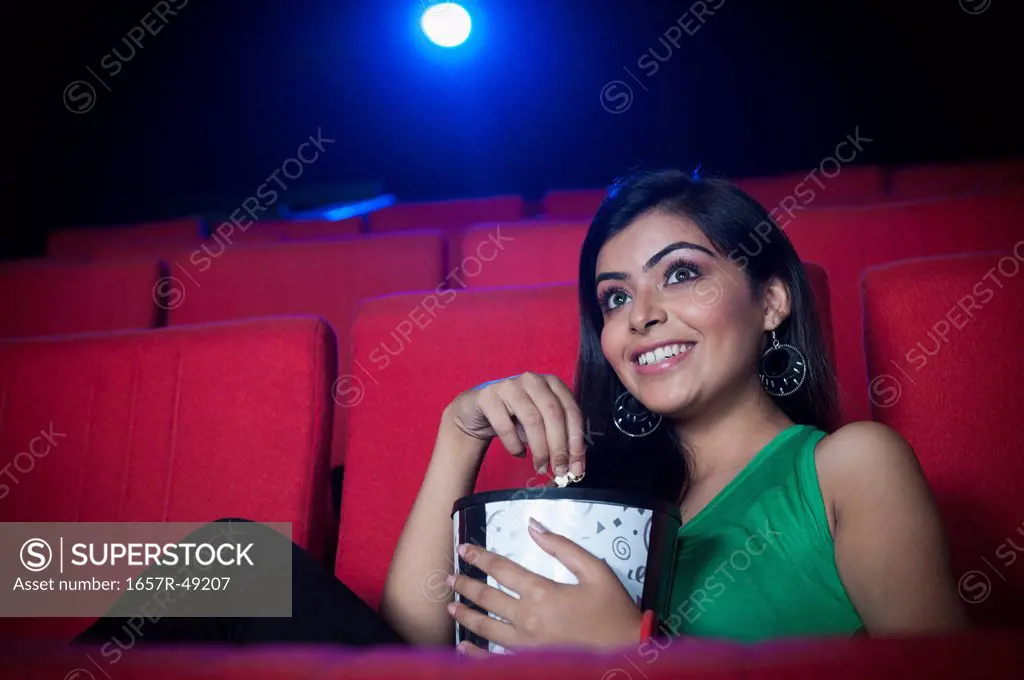 Woman enjoying movie with popcorns in a cinema hall