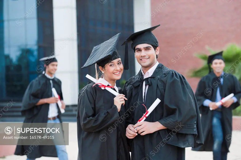 Portrait of graduate students holding diplomas and smiling in university campus