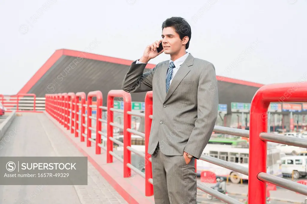 Businessman standing on a footbridge and talking on a mobile phone, Gurgaon, Haryana, India
