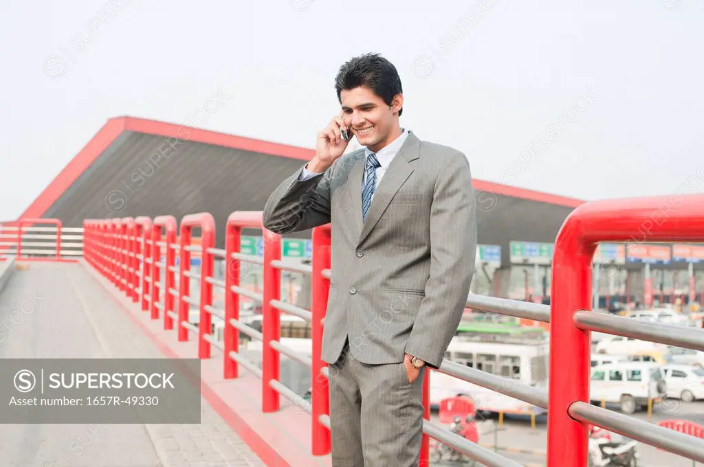 Businessman standing on a footbridge and talking on a mobile phone, Gurgaon, Haryana, India