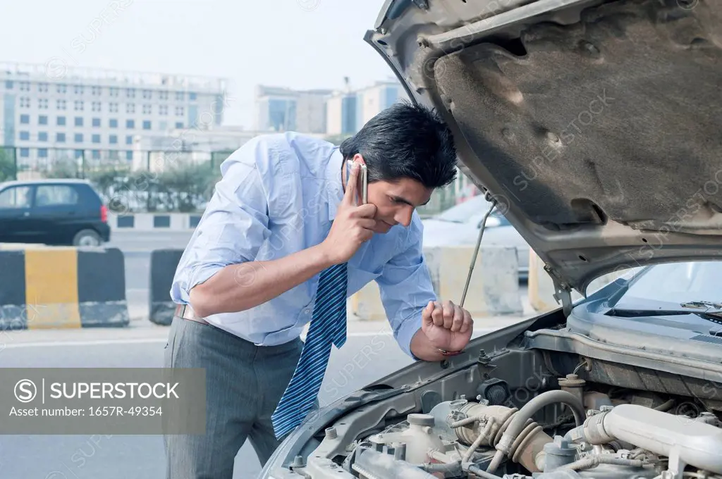 Businessman using a mobile phone near a broken down car, Gurgaon, Haryana, India