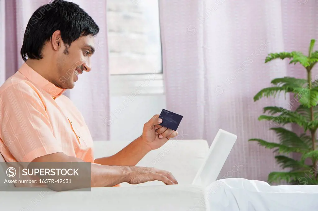 Bengali man using a laptop and holding a credit card