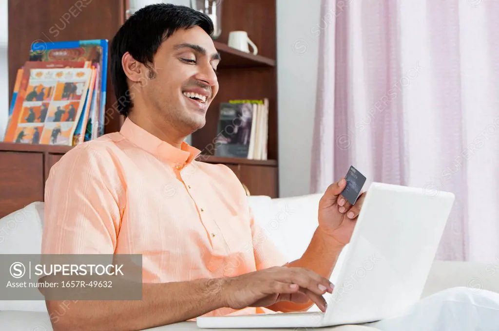 Bengali man using a laptop and holding a credit card