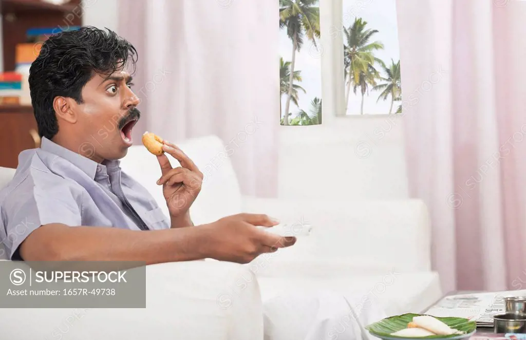 South Indian man watching TV and having food