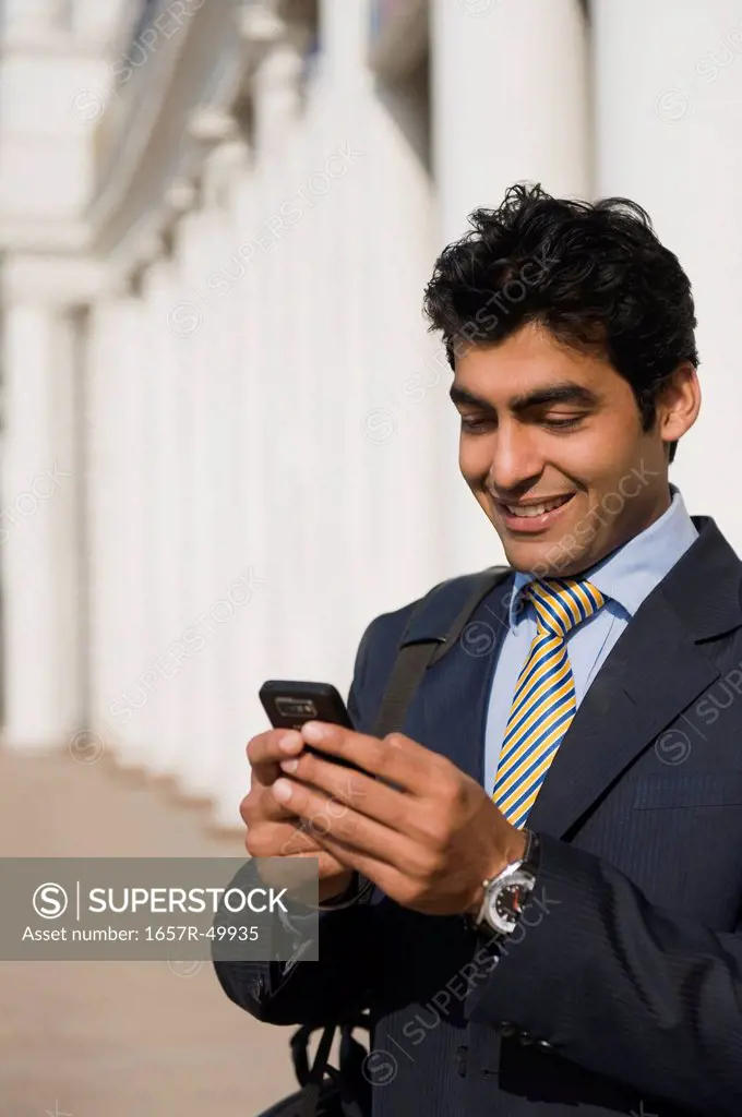 Close-up of a businessman text messaging on a mobile phone and smiling, Gurgaon, Haryana, India