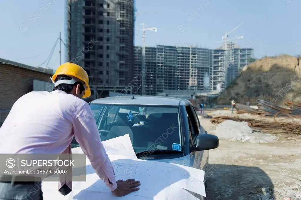 Architect looking at a blueprint at a construction site, Gurgaon, Haryana, India