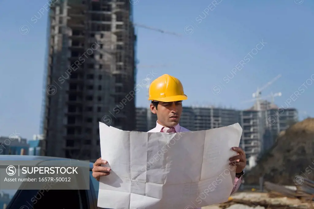 Architect looking at a blueprint at a construction site, Gurgaon, Haryana, India