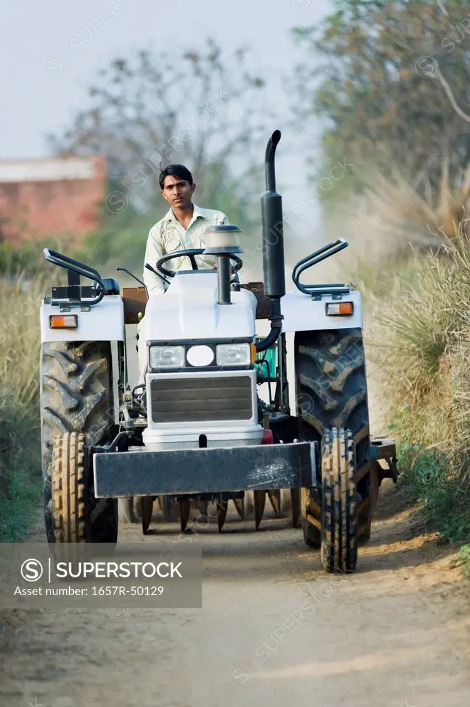 Farmer driving a tractor on a dirt road, Farrukh Nagar, Gurgaon, Haryana, India