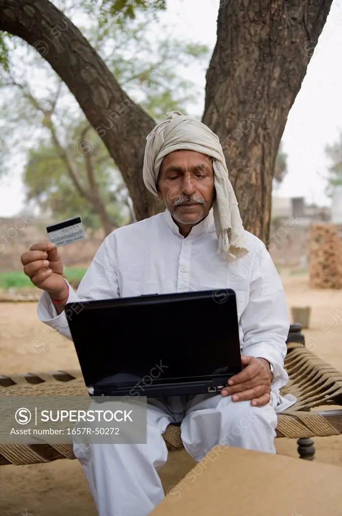 Farmer holding a credit card and using a laptop, Hasanpur, Haryana, India