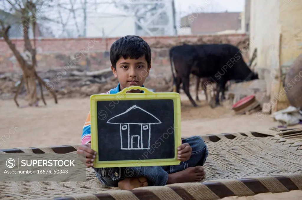 Portrait of a boy showing chalk drawing of house on a slate, Hasanpur, Haryana, India