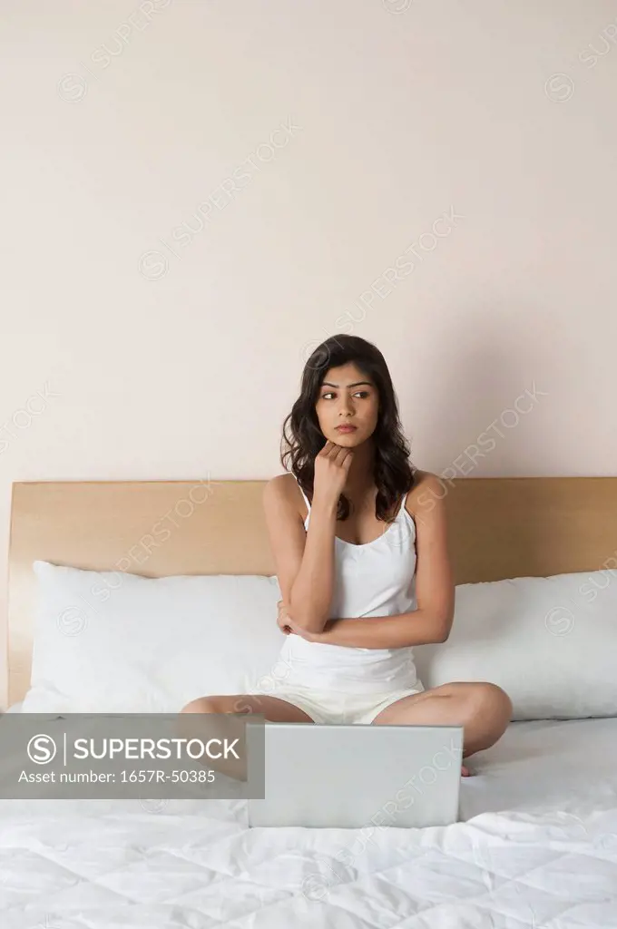 Woman thinking in front of a laptop on the bed