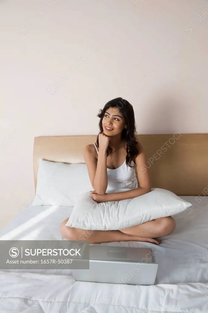 Woman day dreaming in front of a laptop on the bed