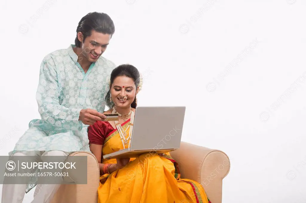 Couple in traditional clothing holding a credit card and using a laptop
