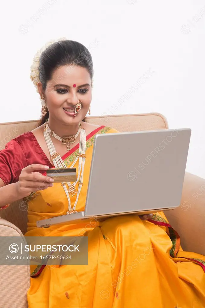 Woman in traditional clothing holding a credit card and using a laptop