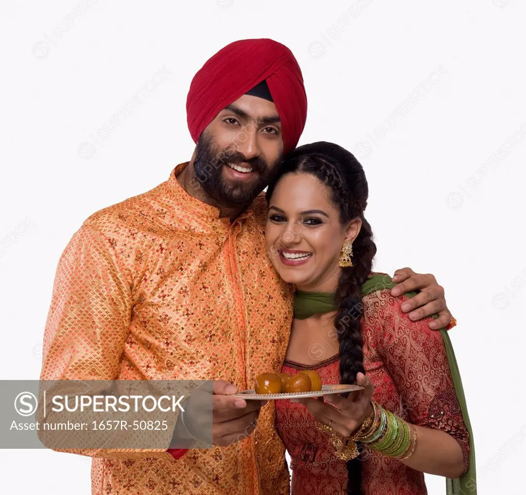 Sikh couple holding a plate of gulab jamuns the traditional Indian sweet