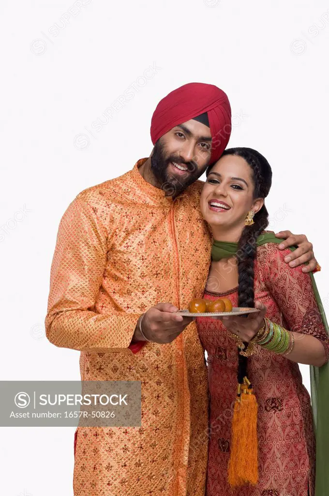 Sikh couple holding a plate of gulab jamuns the traditional Indian sweet