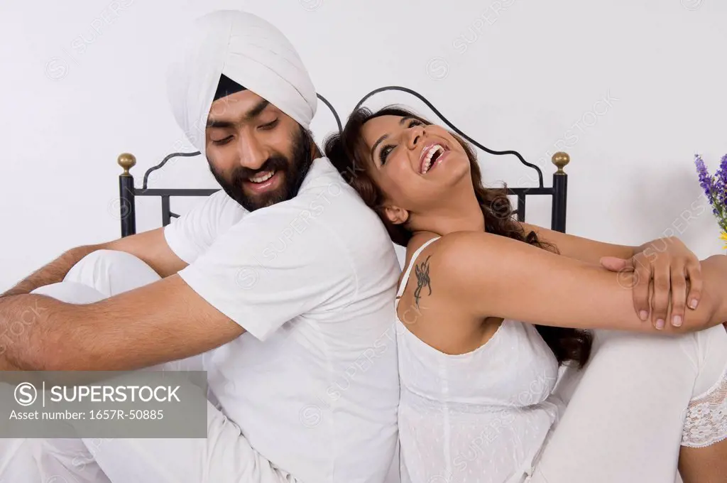 Sikh couple sitting back to back on the bed