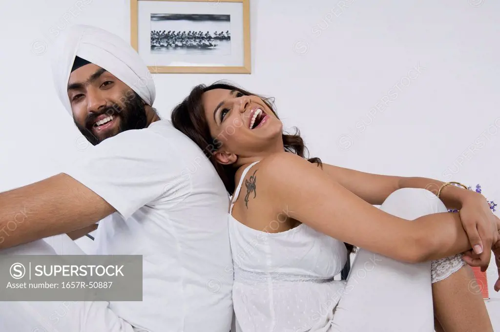 Sikh couple sitting back to back on the bed