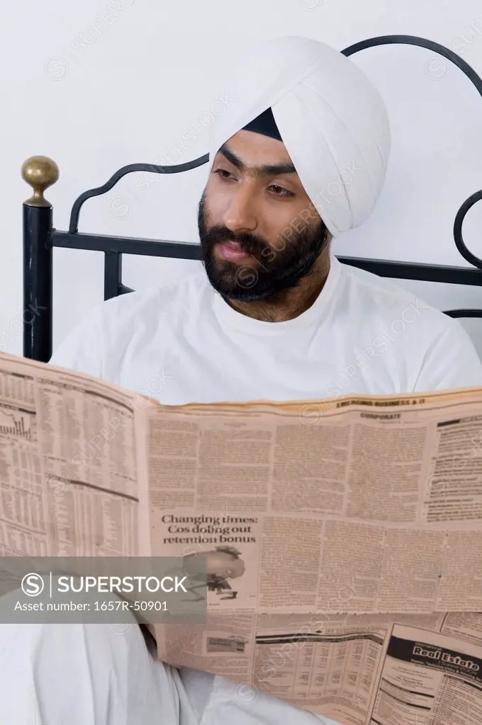 Sikh man reading a newspaper on the bed