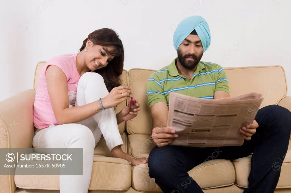 Sikh man reading a newspaper and a woman painting her fingernails