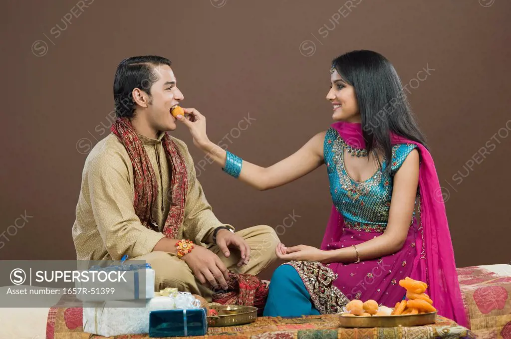Woman feeding sweets to her brother at Raksha Bandhan festival