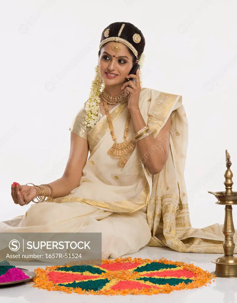 Indian woman in traditional clothing making rangoli and talking on a mobile phone
