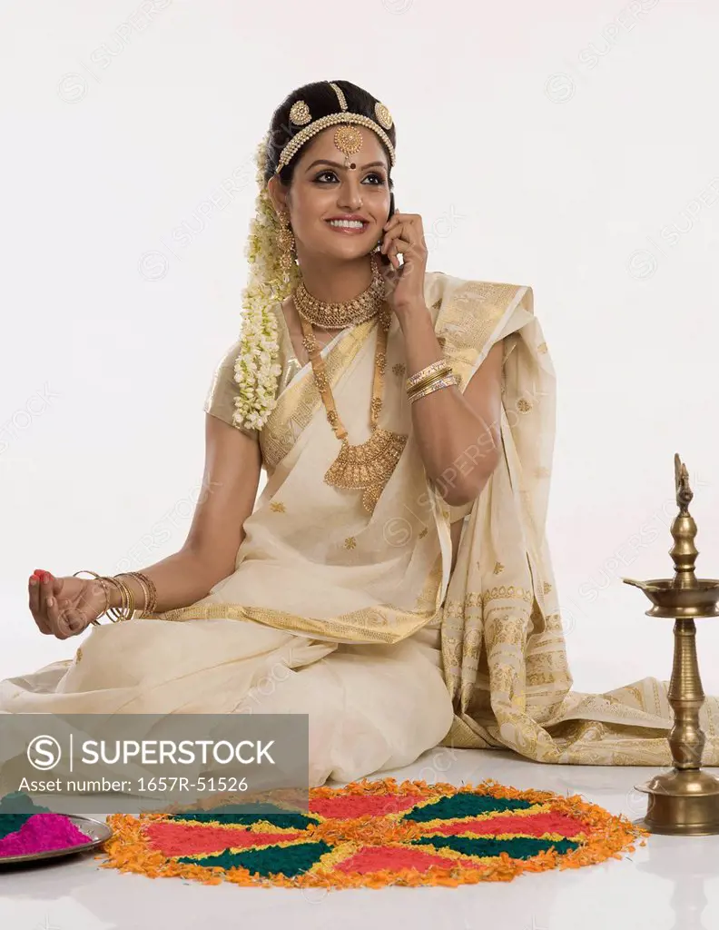 Indian woman in traditional clothing making rangoli and talking on a mobile phone