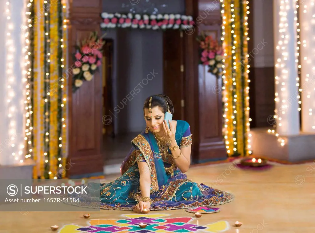 Woman talking on a mobile phone and arranging oil lamps on rangoli