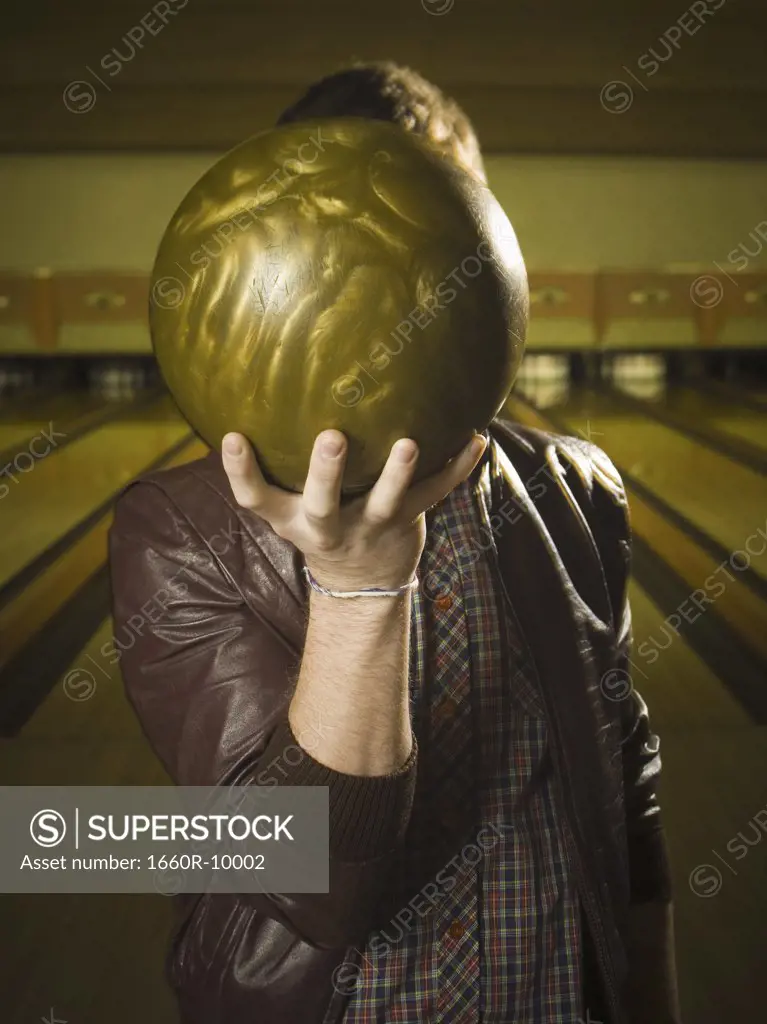 Close-up of a young man holding a bowling ball to his face