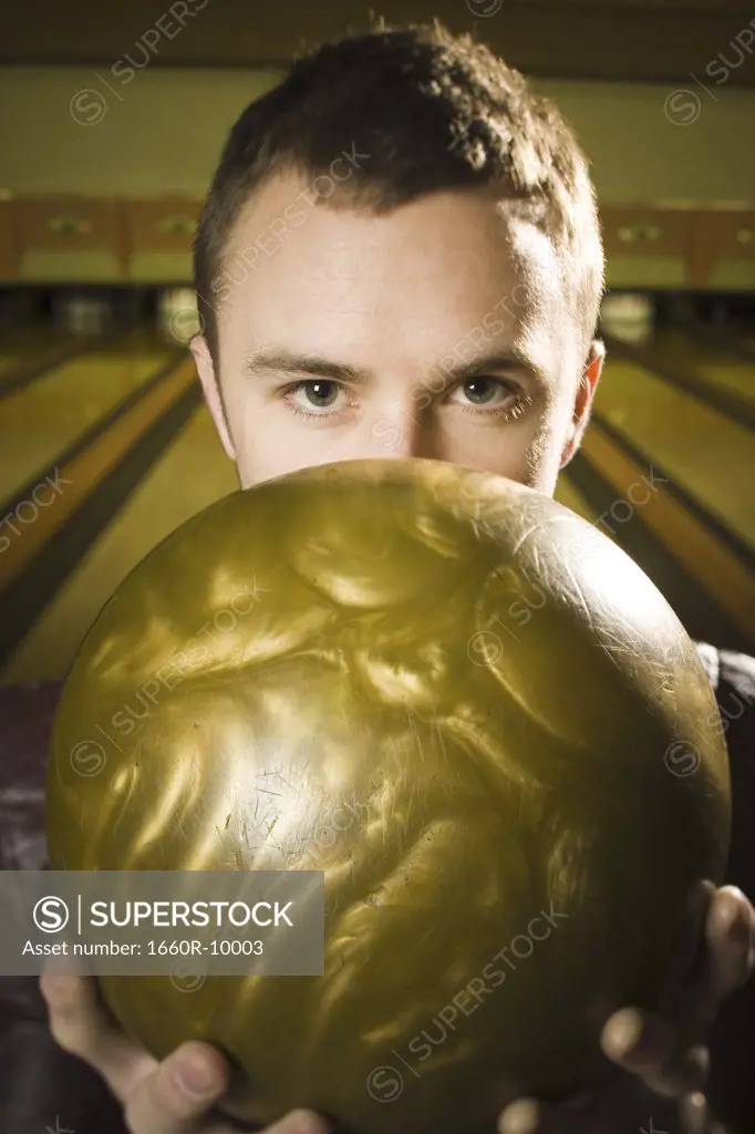 Portrait of a young man holding a bowling ball to his face